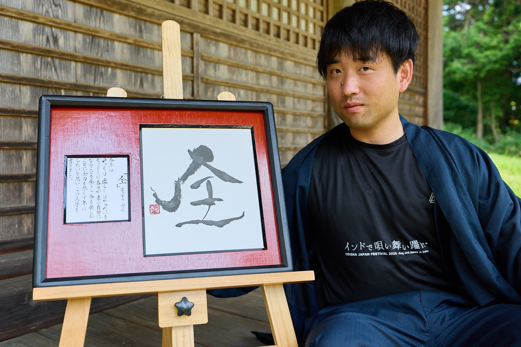 額装作品「全」とともに縁側に座る書家 森下友喜