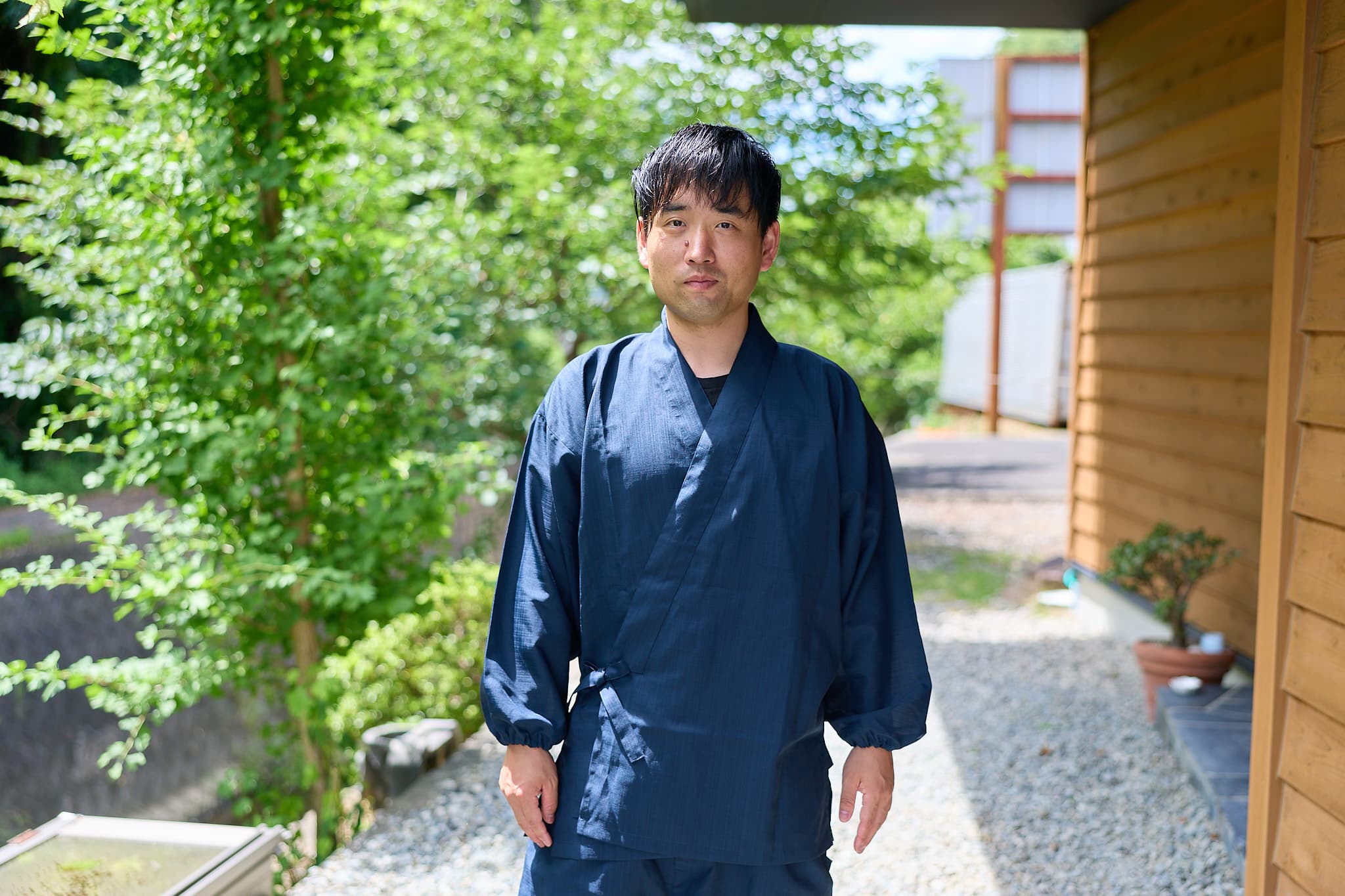 緑の庭先に立つ、作務衣姿の森下友喜