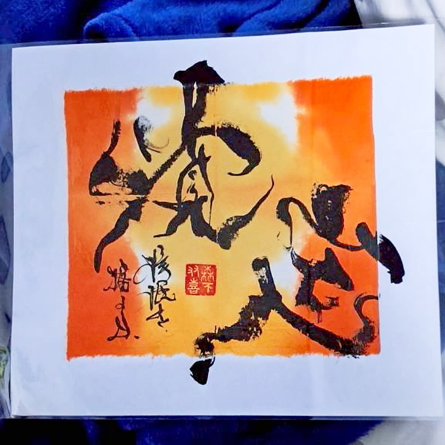 橙と黄に彩色した地に黒墨で二字「覚定」を書いた色紙