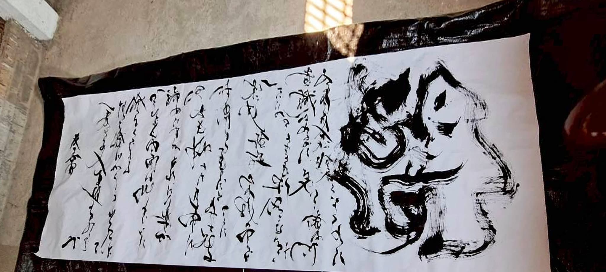 土間で長尺紙に草書の本文と大字「闇」を記した作品