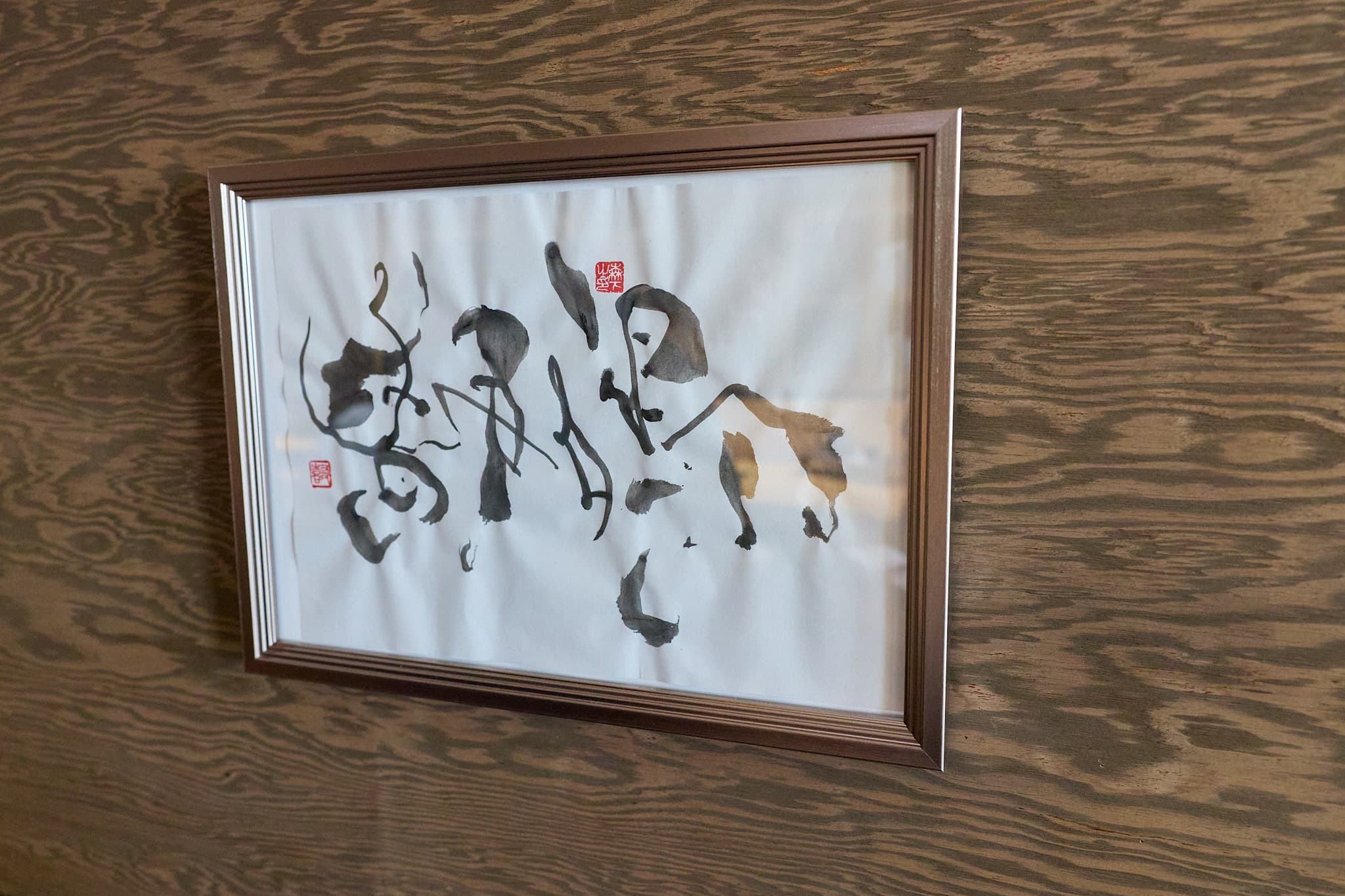 木目の壁に掛けた額装の墨書「静鳴」。朱の落款が二顆押されている
