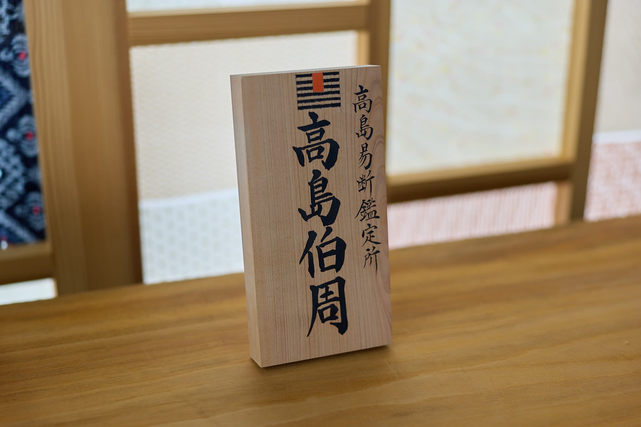 檜の木札に「高島伯周」「高島易断鑑定所」と揮毫し、易の卦を朱で配したサイン
