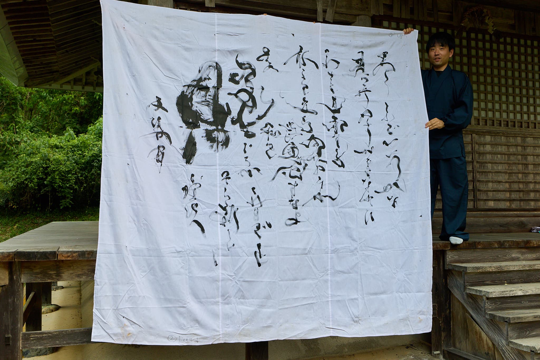 白布いっぱいに揮毫した大型書道作品を、作務衣姿の森下友喜が掲げる様子